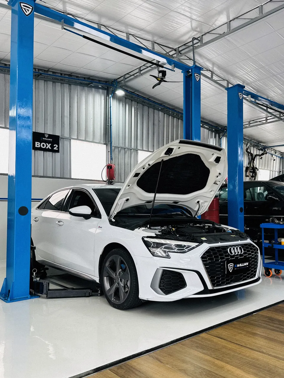 Audi A3 branco com capô aberto, no elevador de duas colunas do Box 2 da oficina.