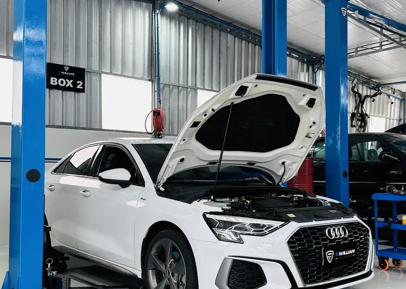 Audi A3 branco com o capô aberto no boxe 2 da oficina.