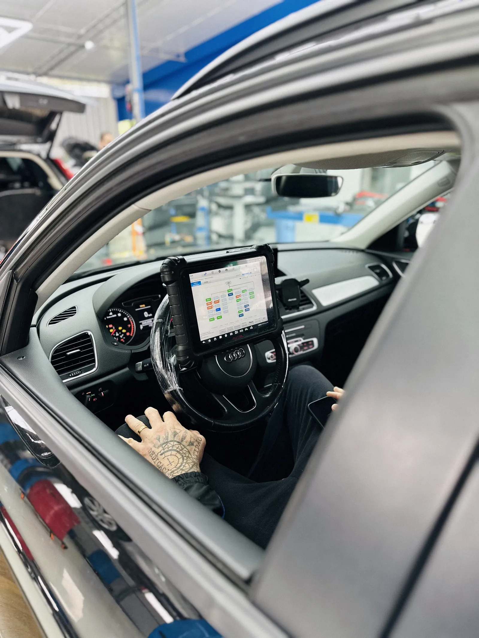 Interior de um Audi com técnico segurando um tablet apoiado no volante