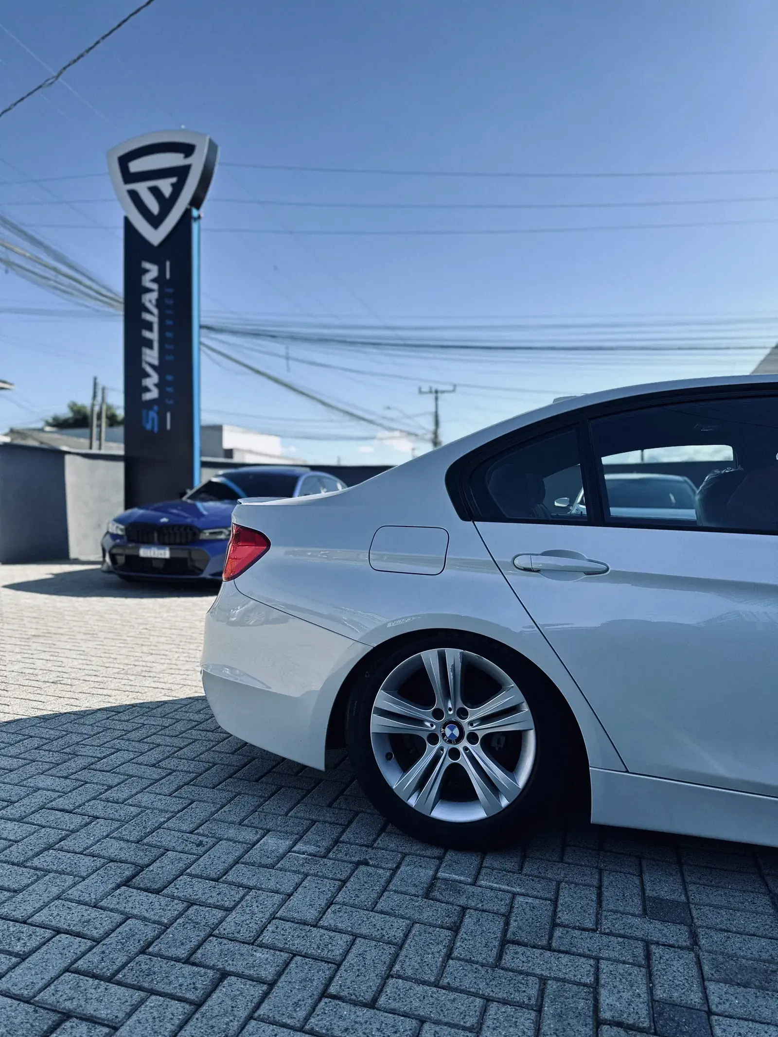 BMW branco visto de perfil no pátio externo de paralelepípedo da oficina.