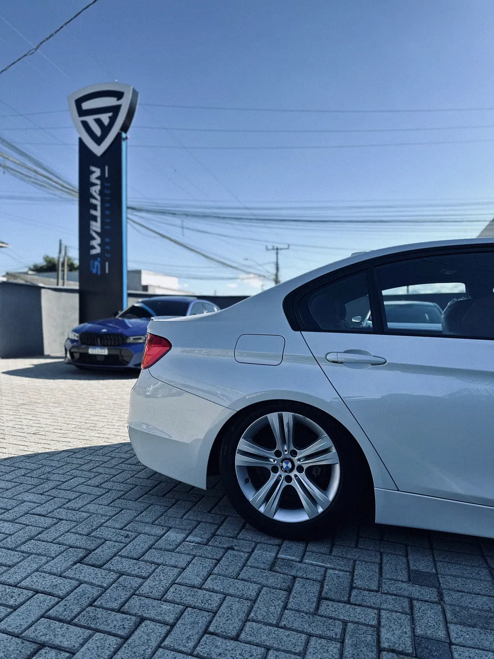 BMW branco visto de perfil no pátio externo de paralelepípedo da oficina.