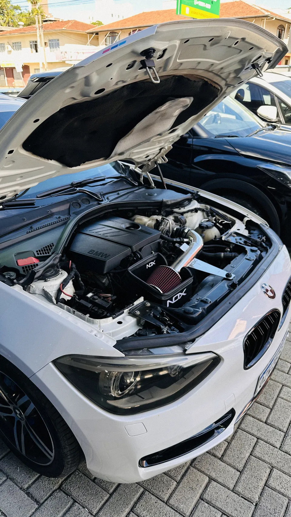 BMW Série 1 com admissão à mostra no pátio externo da oficina.
