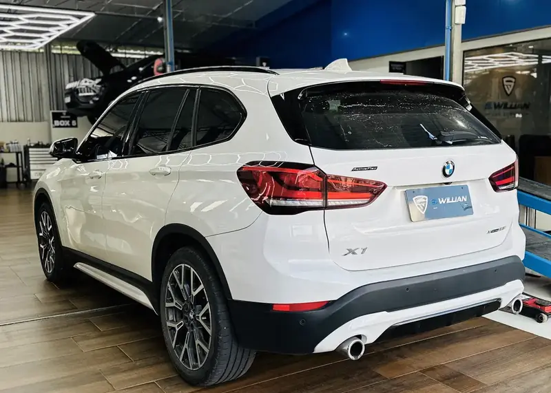 BMW X1 branco visto de trás sob o teto hexagonal de LED da oficina.