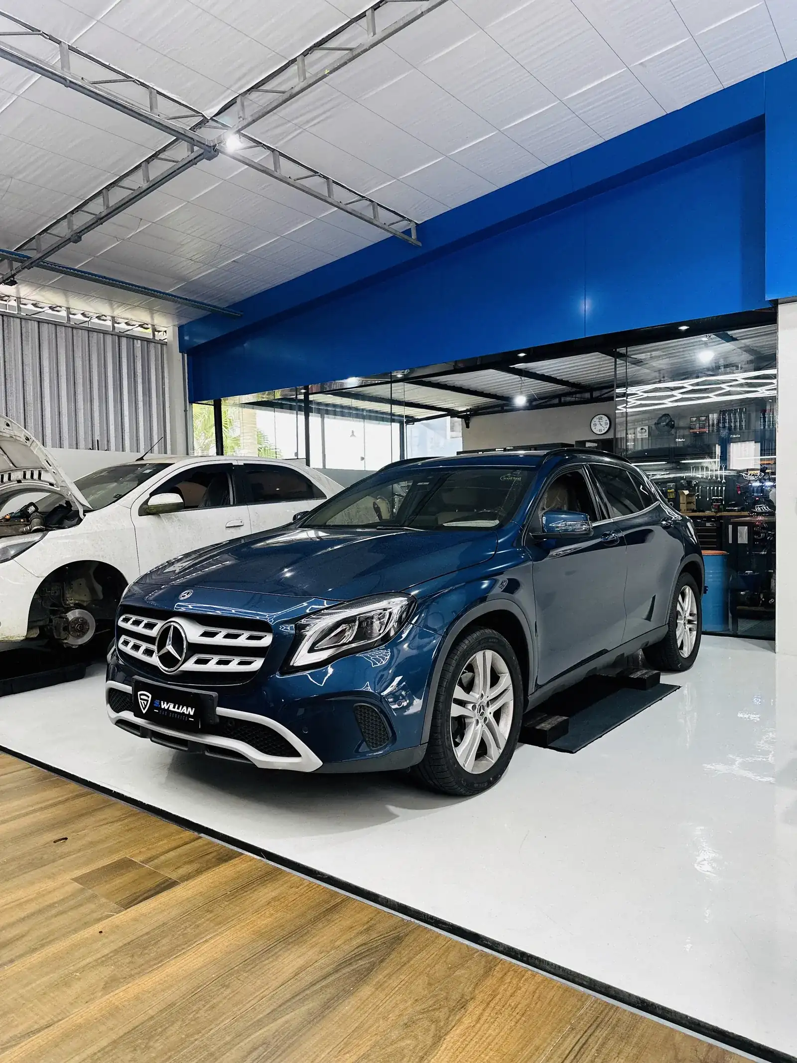 Mercedes-Benz GLA na recepção da oficina, próximo à entrada, com piso de madeira e chão branco.