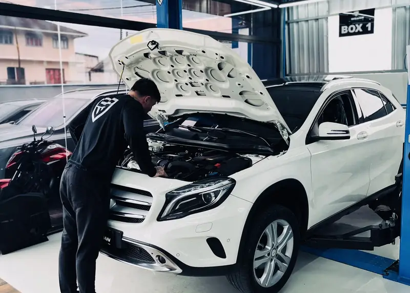 Técnico da oficina mexendo no motor de um Mercedes-Benz GLA branco, no Box 1.