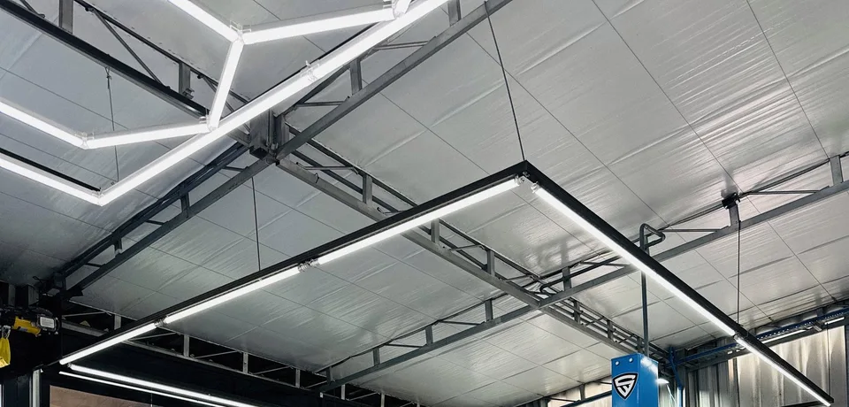Teto da oficina com as luminárias de LED e a estrutura metálica sobre o box, com o escudo da S. Willian na coluna do elevador.