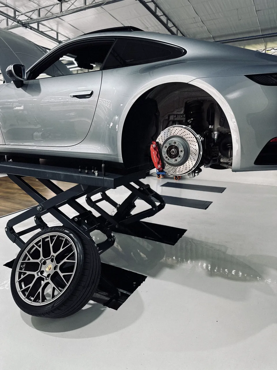 Detalhe da roda e do disco de freio de um Porsche 911 no elevador tesoura da oficina.