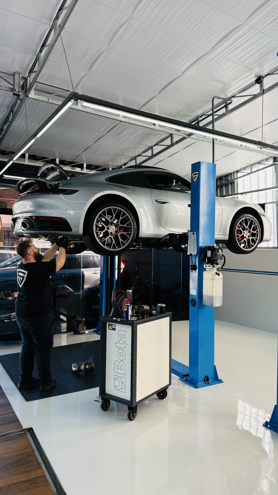 Porsche 911 no elevador da oficina, com o técnico trabalhando embaixo.