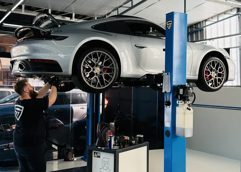 Porsche 911 no elevador da oficina, com o técnico trabalhando embaixo.