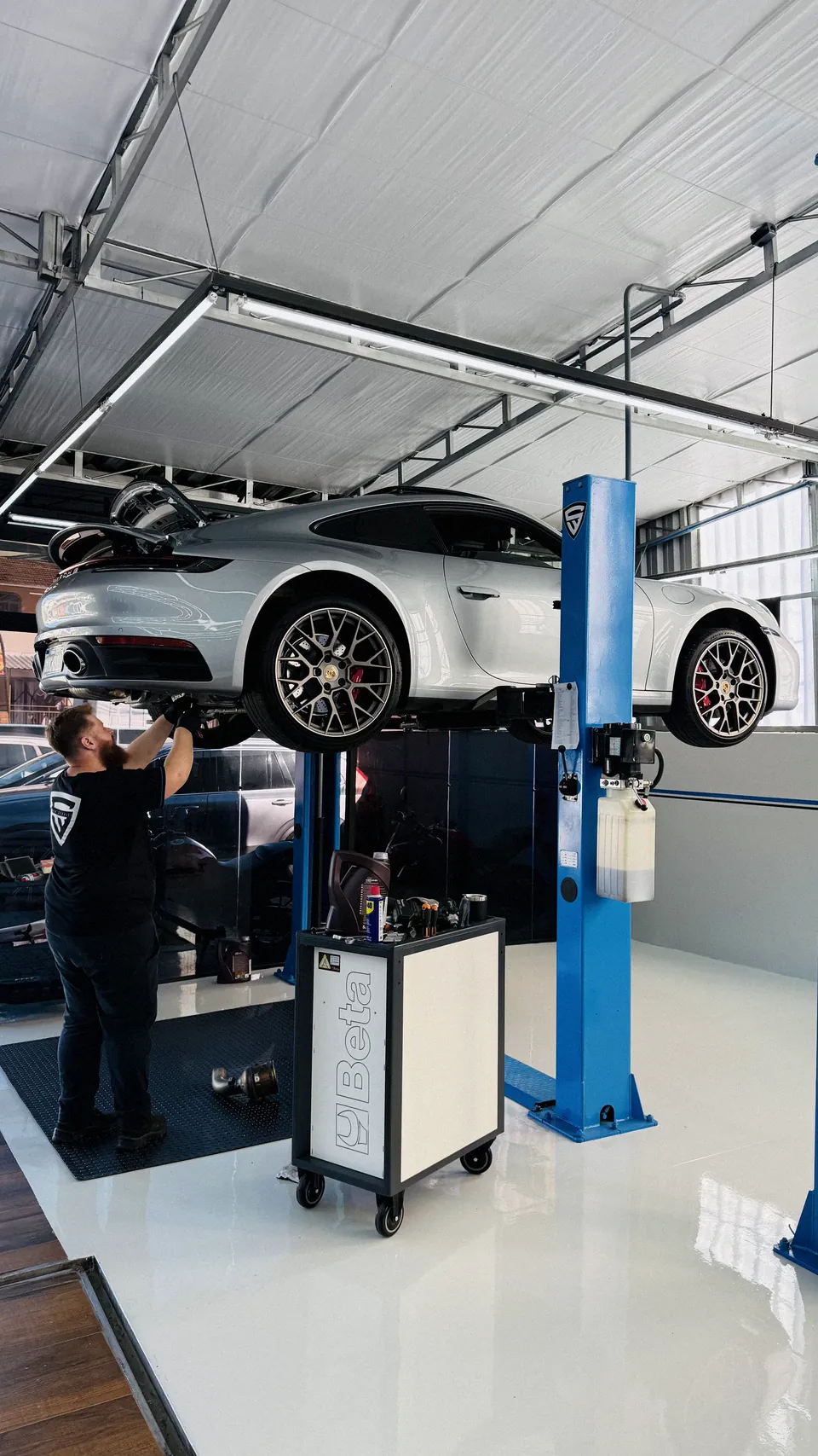 Porsche 911 no elevador de duas colunas, com técnico trabalhando na roda.