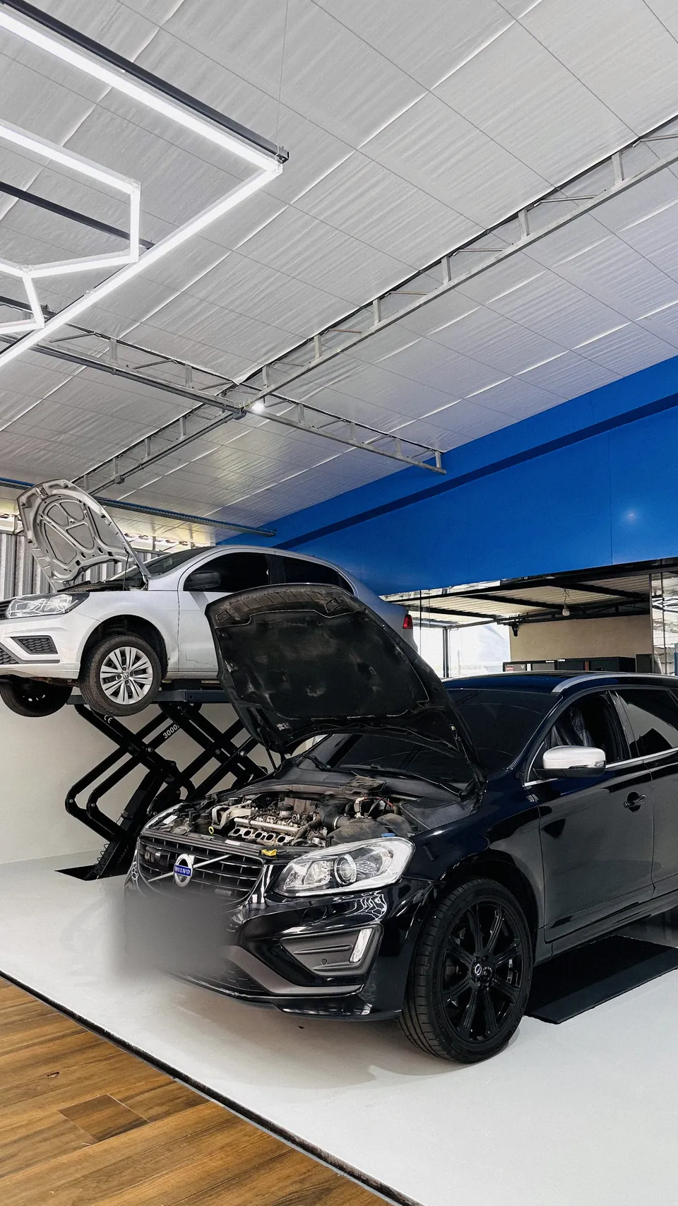 Volvo XC60 preto em primeiro plano, com outro XC60 prata ao fundo, sob teto hexagonal de LED.
