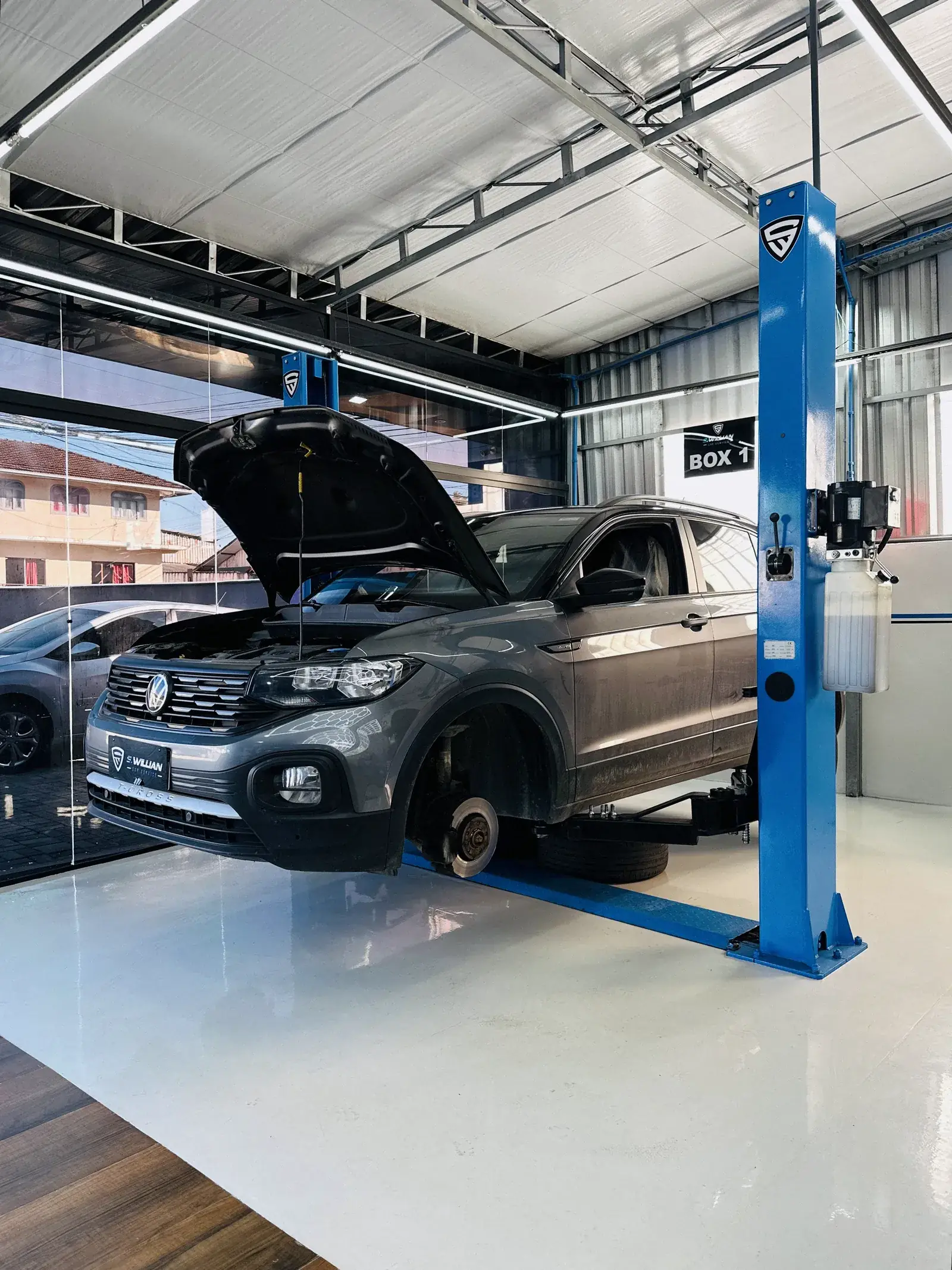 Volkswagen T-Cross cinza no elevador com o capô aberto e a roda removida, freio à vista